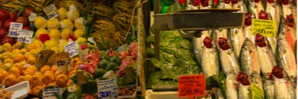 Colorful outdoor market with fresh fruits, vegetables, and fish available for sale.