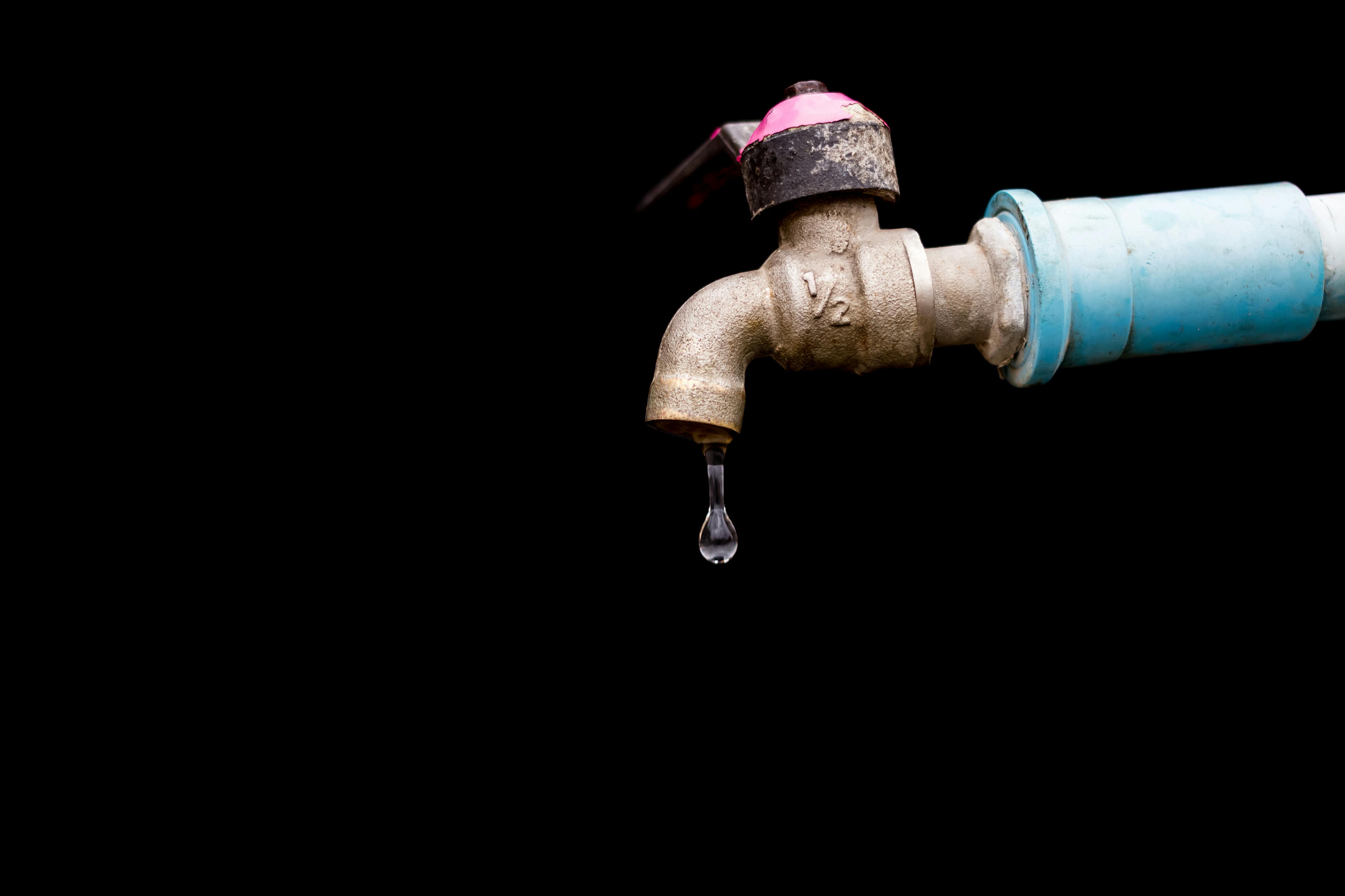 A detailed view of a metal faucet with a single water drop against a black background.